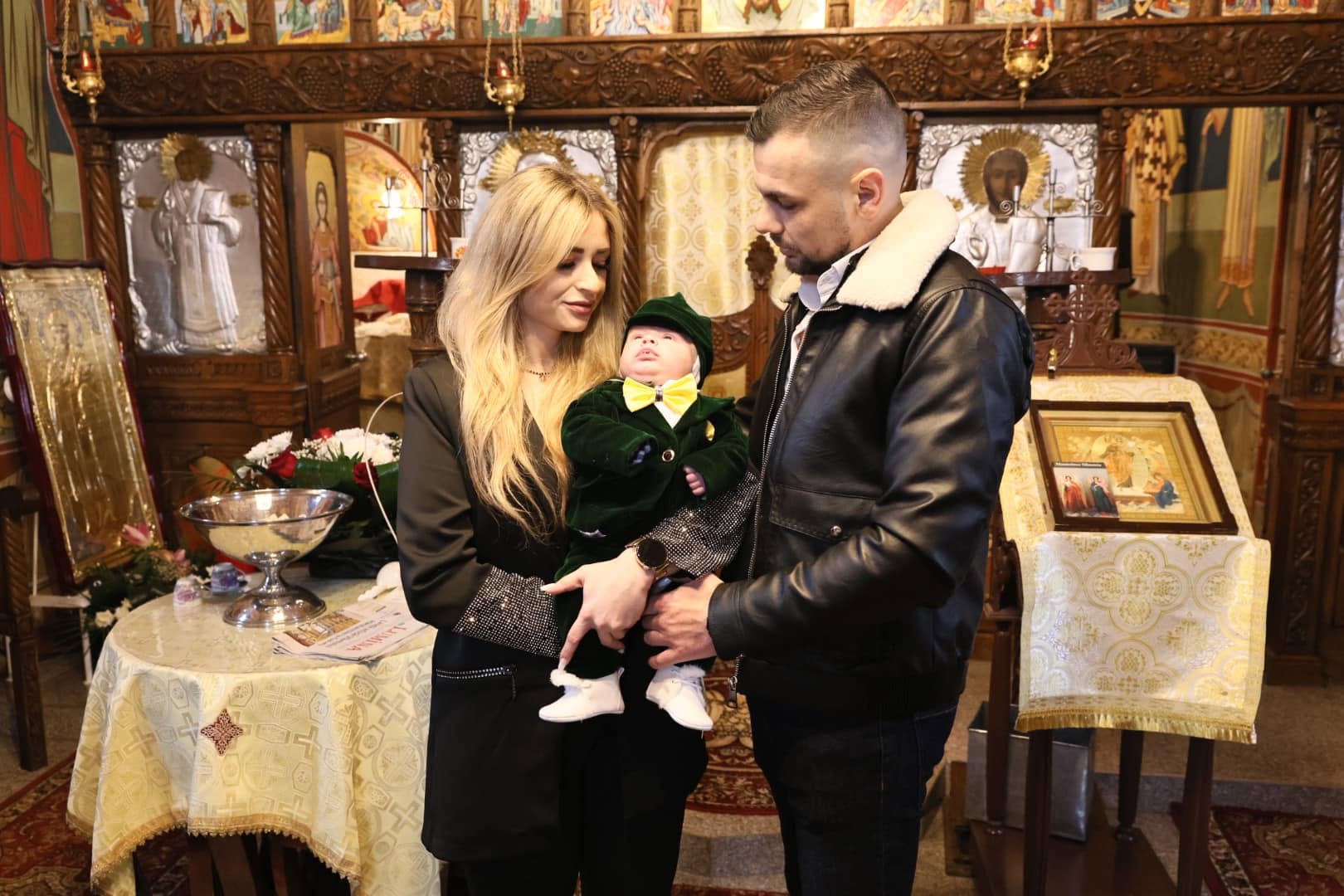 Părinți cu bebelușul în costum verde la altar